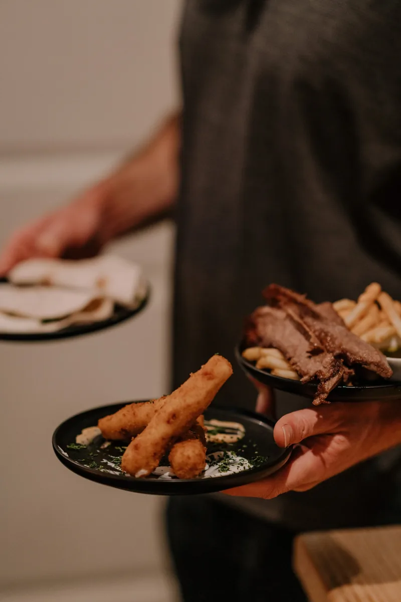 A server setting down plates of croquetas and charcuterie
